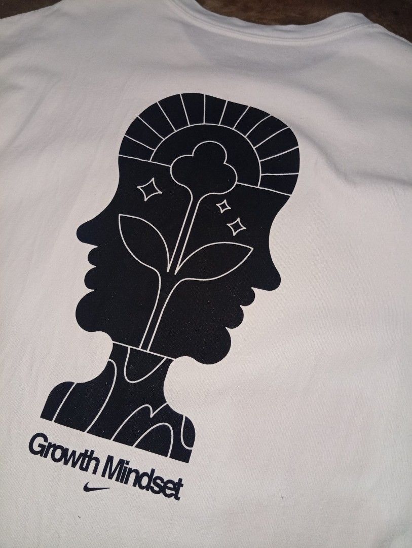 Nike Growth Mindset Graphic White T-Shirt (Category: Tshirts & Polo Shirts ) located in Legazpi City. Submitted by thriftfinds-25 (Listing ID 1466054352, Image 3). Description: White Nike graphic tee with classic black swoosh logo on the front chest. Back has a large abstract two-faced head illustration with a growing plant, sun rays, stars, and 'Growth Mindset' lettering above a tiny swoosh. Small Nike Sunburst logo tag sewn on the lower front h