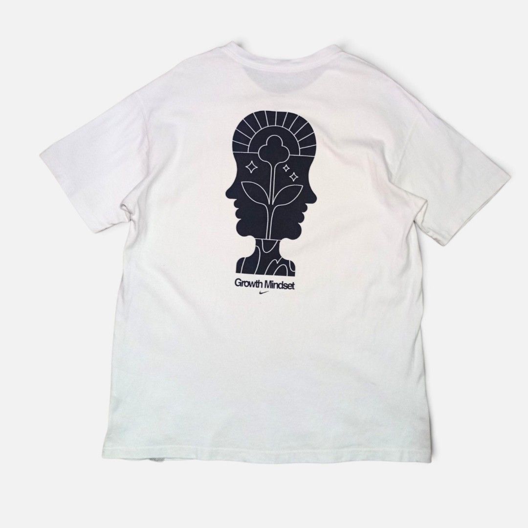 Nike Growth Mindset Graphic White T-Shirt (Category: Tshirts & Polo Shirts ) located in Legazpi City. Submitted by thriftfinds-25 (Listing ID 1466054352, Image 1). Description: White Nike graphic tee with classic black swoosh logo on the front chest. Back has a large abstract two-faced head illustration with a growing plant, sun rays, stars, and 'Growth Mindset' lettering above a tiny swoosh. Small Nike Sunburst logo tag sewn on the lower front h