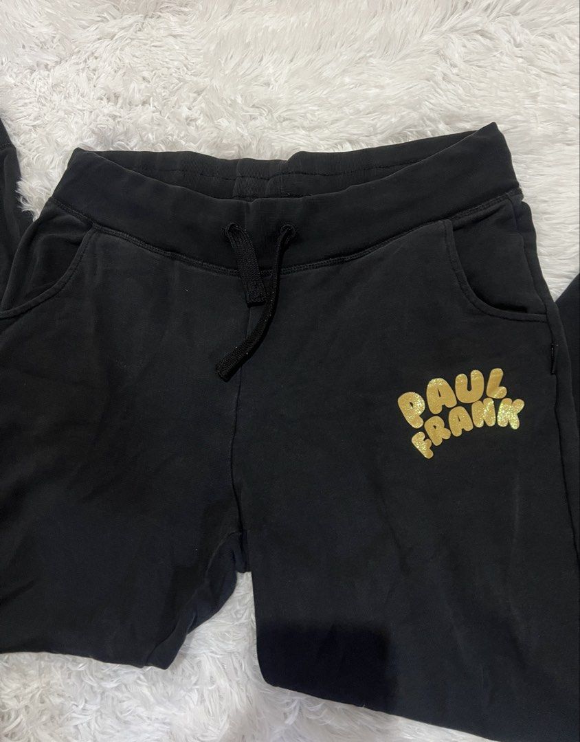 Paul Frank Black Gold Glitter Sweatpants (Category: Joggers) located in Tuguegarao City. Submitted by love_clothies (Listing ID 1465968570, Image 2). Description: - Brand: Paul Frank - Color: Black with shiny gold glitter logo on the left leg - Material: Soft, comfortable cotton - Features: Elastic waistband, black drawstring, side pockets, and ribbed ankle cuffs - Condition: In solid shape overall - Best for: Lounging at home or casual daily err