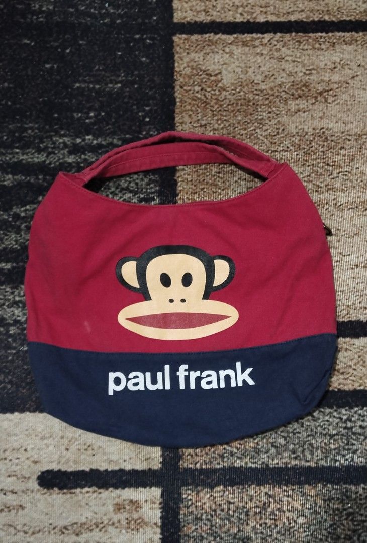 Paul Frank Canvas Handbag Red and Navy Blue (Category: Tote Bags) located in Manila. Submitted by ianmontede19006 (Listing ID 1466010239, Image 1). Description: - Authentic Paul Frank canvas handbag in red and navy blue - Features the iconic Julius the monkey face graphic on the front - White Paul Frank text logo accent on the lower navy section - Comfortable curved handle strap design with soft fabric construction - Compact size, ideal for daily