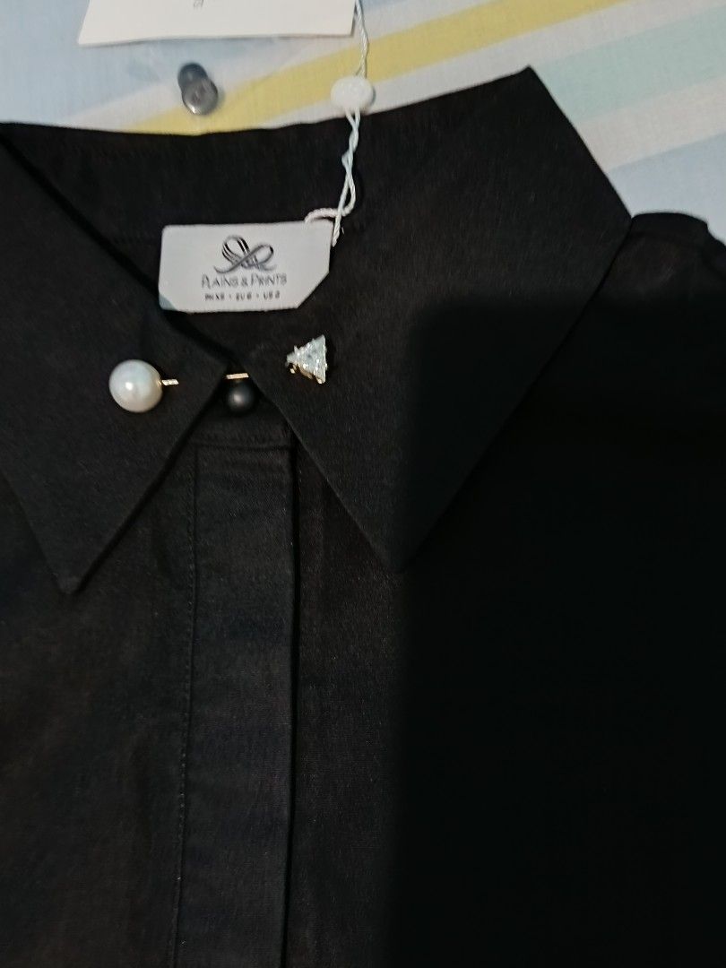 Plains & Prints Black Long Sleeve Blouse (Category: Longsleeves) located in Aroroy. Submitted by new_annette (Listing ID 1465982493, Image 2). Description: - Brand: Plains & Prints - Color: Classic Black - Style: Long sleeve blouse with collar and button cuffs - Details: Pearl and crystal decorative pins near the neckline, gold ribbon logo hardware on the back collar - Condition: Brand new with tag attached - Ideal for: Office wear, corporate eve