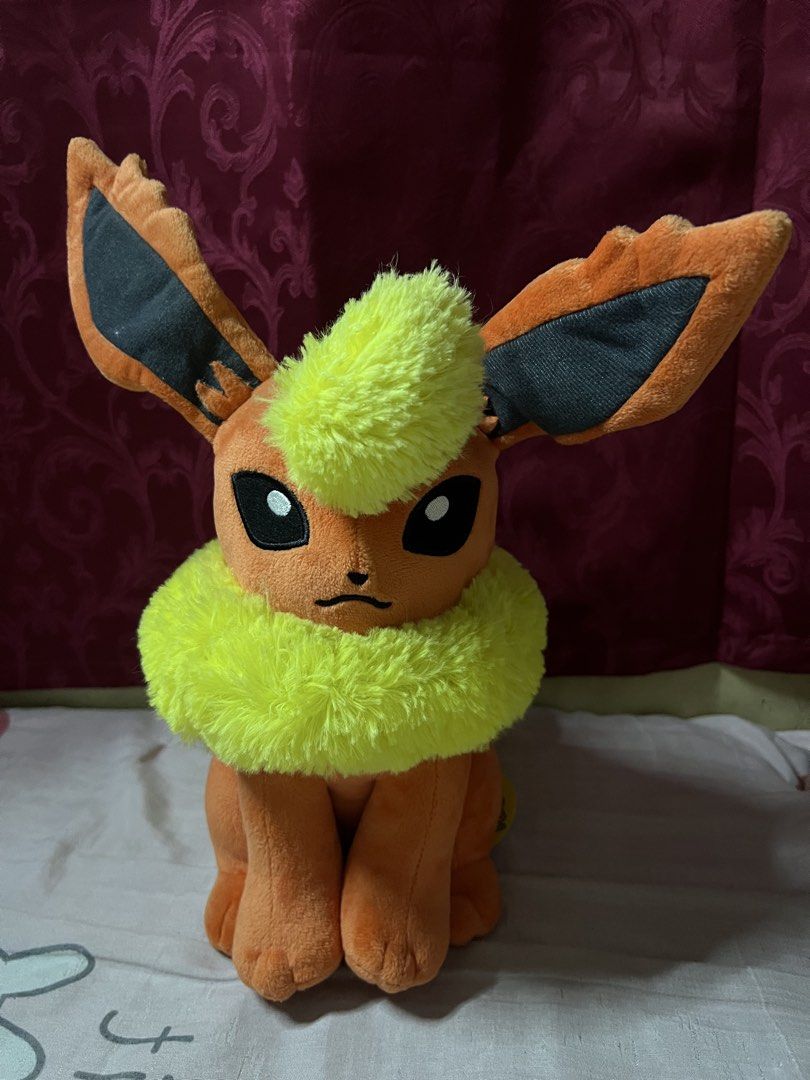 Pokemon Flareon Plush Toy (Category: Plushies & Soft Toys) located in Bulacan. Submitted by haven_plushie_dolls.888 (Listing ID 1466080296, Image 1). Description: - Official Pokémon Flareon plush toy - Soft orange fabric with vibrant yellow fluff on neck and tail - Large pointy ears with dark inner details - Sits upright independently - Includes original yellow hang tag and white tush tag - Clean and well-maintained collector's item.