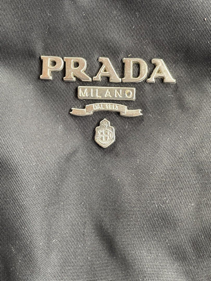Prada Black Nylon Handbag (Category: Luxury Bags & Wallets) located in Zamboanga. Submitted by stephoney03 (Listing ID 1466037330, Image 3). Description: - black nylon Prada handbag - Silver-tone hardware with iconic front metal logo lettering - Adjustable single black strap with buckle and clasp detail - Secure top zipper closure - Interior lined with signature Prada logo fabric - Inner leather brand tag (Note: shows scuffs and noticeable wear o
