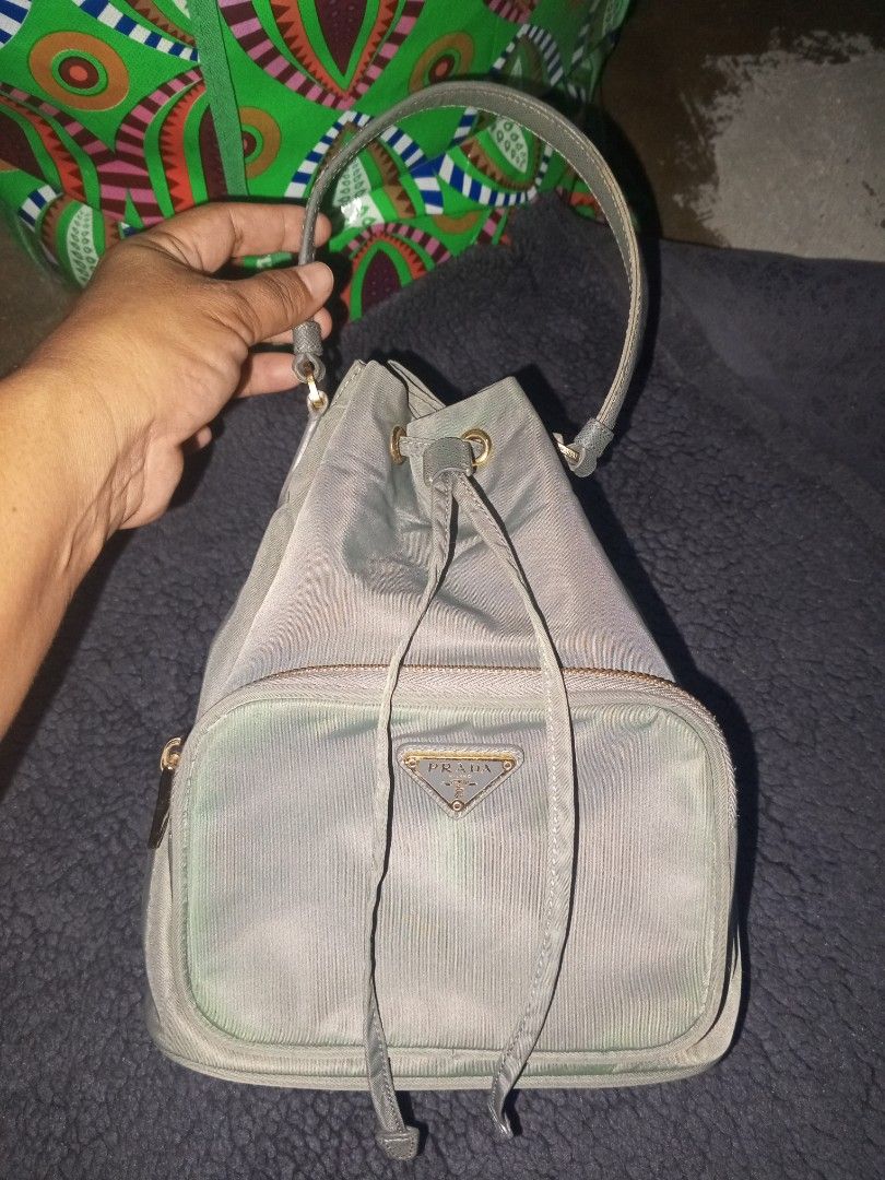 Prada Nylon Bucket Bag (Category: Luxury Bags & Wallets) located in Magalang. Submitted by zeiansoria64090 (Listing ID 1466083605, Image 1). Description: - Authentic Prada nylon bucket bag - Features a convenient top handle and secure drawstring closure - Front zipper pocket accented with the iconic metal triangle logo - Luxurious gold-tone hardware, including Lampo zippers and engraved handle rings - Spacious interior with practical compartments