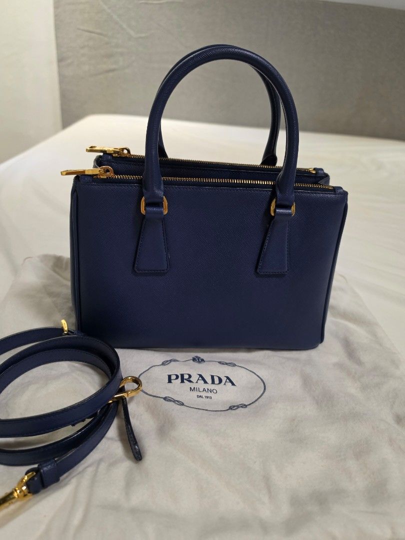 Prada Saffiano Galleria (Category: Luxury Bags & Wallets) located in Paranaque City. Submitted by decluttering_by_anna (Listing ID 1466076820, Image 2). Description: - Rich navy blue Prada Saffiano Galleria double-zip tote, highlighted by its signature gold-tone triangular logo plaque. - Authentic - Elegant gold-tone hardware and iconic triangular Prada logo plaque - Structured silhouette with top handles and snap buttons on the sides - Double zi