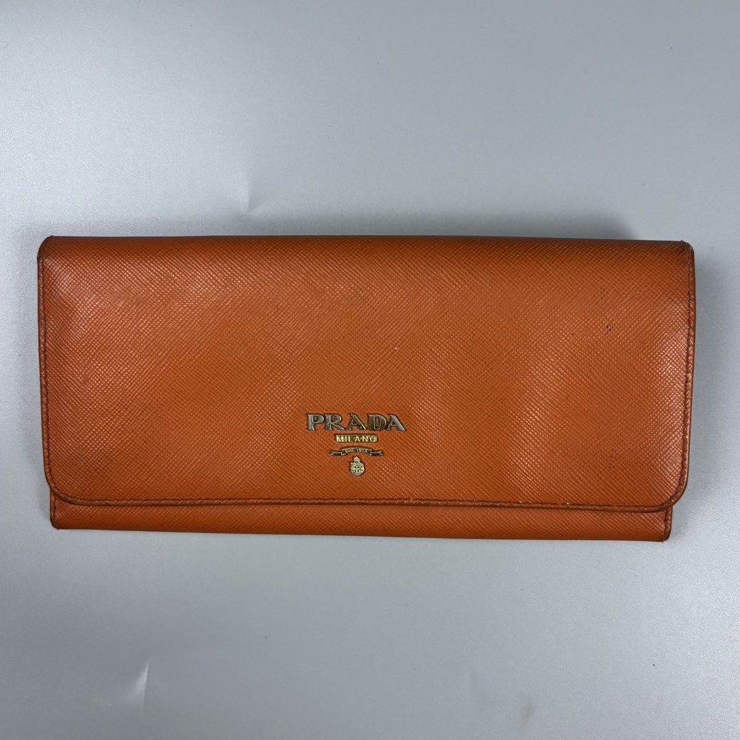 Prada Saffiano Leather Long Wallet Orange (Category: Wallets & Card holders) located in Mabalacat. Submitted by doughnutthrift (Listing ID 1466110022, Image 2). Description: - Prada long wallet crafted from vibrant orange Saffiano leather - Mixed gold and silver-tone hardware with iconic Prada lettering logo - Convenient zipped exterior coin compartment - Multiple interior card slots for easy organization - Made in Italy - Includes original authe