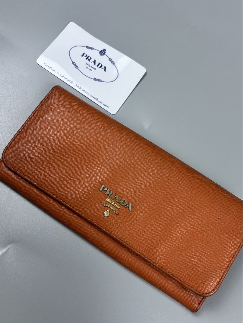 Prada Saffiano Leather Long Wallet Orange (Category: Wallets & Card holders) located in Mabalacat. Submitted by doughnutthrift (Listing ID 1466110022, Image 1). Description: - Prada long wallet crafted from vibrant orange Saffiano leather - Mixed gold and silver-tone hardware with iconic Prada lettering logo - Convenient zipped exterior coin compartment - Multiple interior card slots for easy organization - Made in Italy - Includes original authe