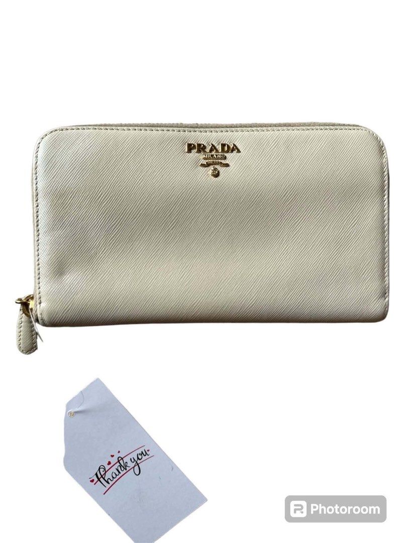 Prada Saffiano Leather Zip Around Wallet (Category: Wallets & Card holders) located in Manila. Submitted by attypreciousyzncpa (Listing ID 1466150018, Image 1). Description: Prada zip-around wallet in cream Saffiano leather. Gold-tone Prada Milano logo plaque centered on the front. Zip closure with gold hardware and a matching leather pull tab. Structured rectangular shape with fine crosshatch texture. Includes original black Prada presentation b