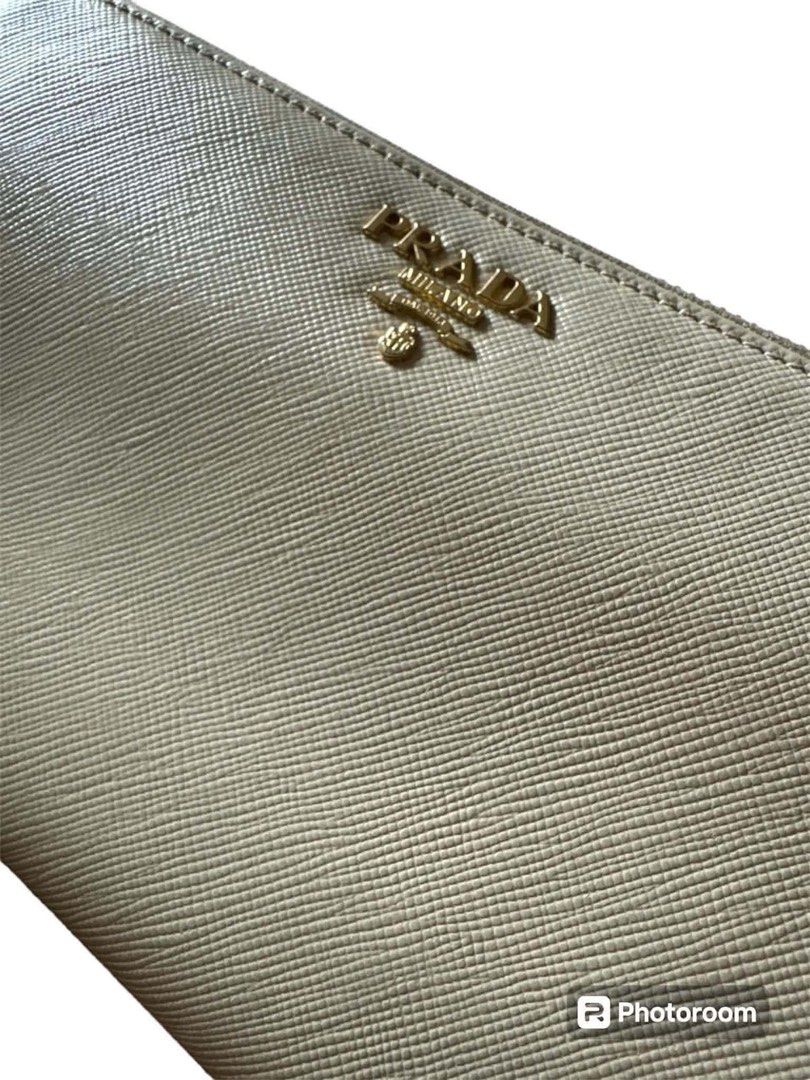 Prada Saffiano Leather Zip Around Wallet (Category: Wallets & Card holders) located in Manila. Submitted by attypreciousyzncpa (Listing ID 1466150018, Image 2). Description: Prada zip-around wallet in cream Saffiano leather. Gold-tone Prada Milano logo plaque centered on the front. Zip closure with gold hardware and a matching leather pull tab. Structured rectangular shape with fine crosshatch texture. Includes original black Prada presentation b