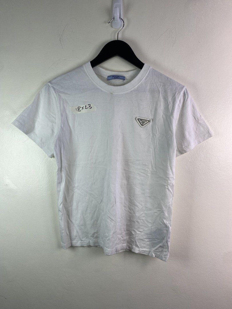 Prada White T-Shirt with Triangle Logo (Category: Shirts) located in Manila. Submitted by declutterpromax (Listing ID 1466028038, Image 1). Description: - Prada white crew neck t-shirt - Iconic metal and enamel triangle logo plaque on left chest - Tagged size M (measurements: 18x23 inches) - Features interior blue Prada Milano neck label and black care tag - Condition: Good overall, with a small yellowish stain near the front collar area as pictu