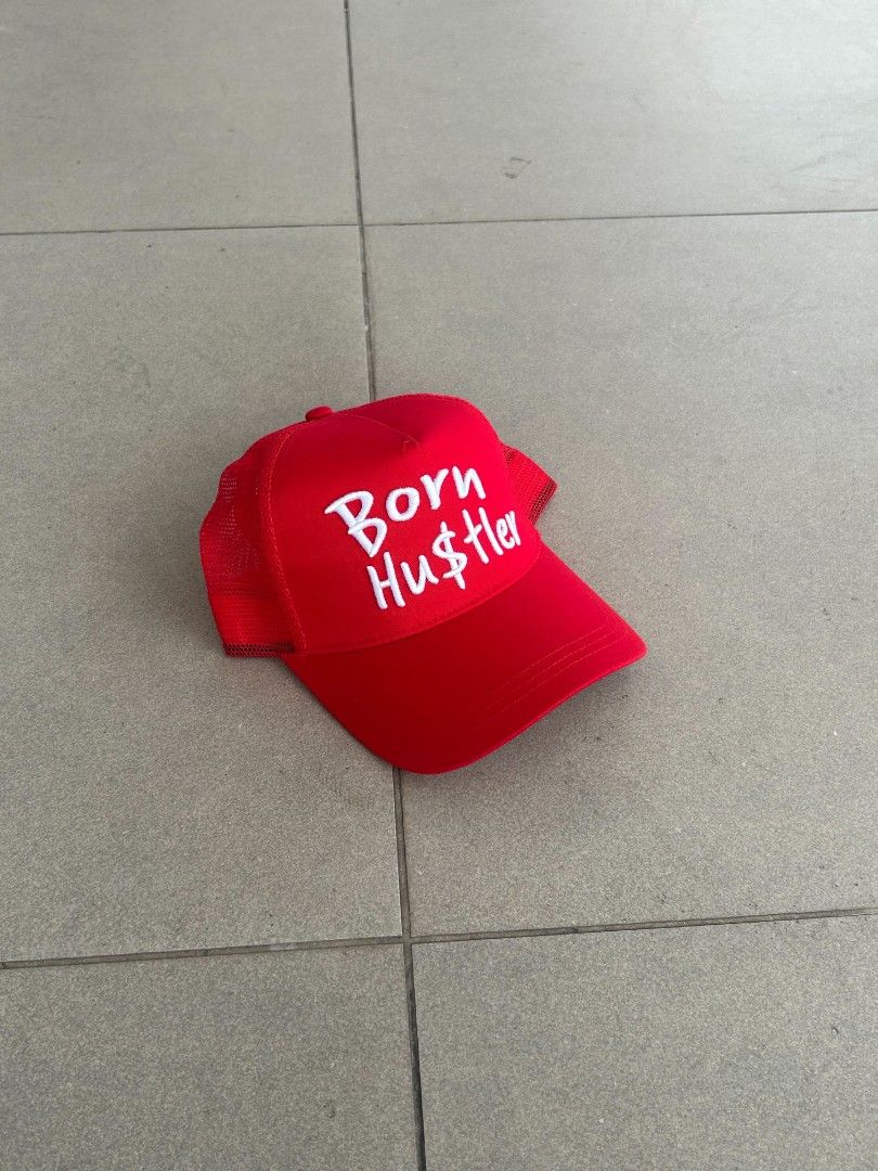 Red Born Hustler Trucker Hat (Category: Caps & Hats) located in Pasig City. Submitted by paulclzdo (Listing ID 1466072378, Image 2). Description: - Color: Vibrant red with white 'Born Hu$tler' embroidered text - Condition: Brand new, never worn - Features: Breathable mesh backing and clean interior lining - Closure: Adjustable snapback for a custom fit - Style: Ideal for casual streetwear and everyday wear.