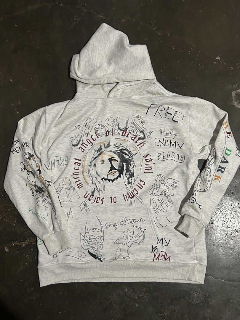 Saint Michael Jesus Print Hoodie (Category: Hoodies) located in Cabuyao City. Submitted by hachikuro (Listing ID 1466039799, Image 1). Description: - Design: Grey pullover hoodie with all-over hand-drawn style illustrations and graphic text - Back Details: Large 'SAINT' lettering paired with an angel graphic 25.5 x27 issue one penhole naka post na po and no tags.