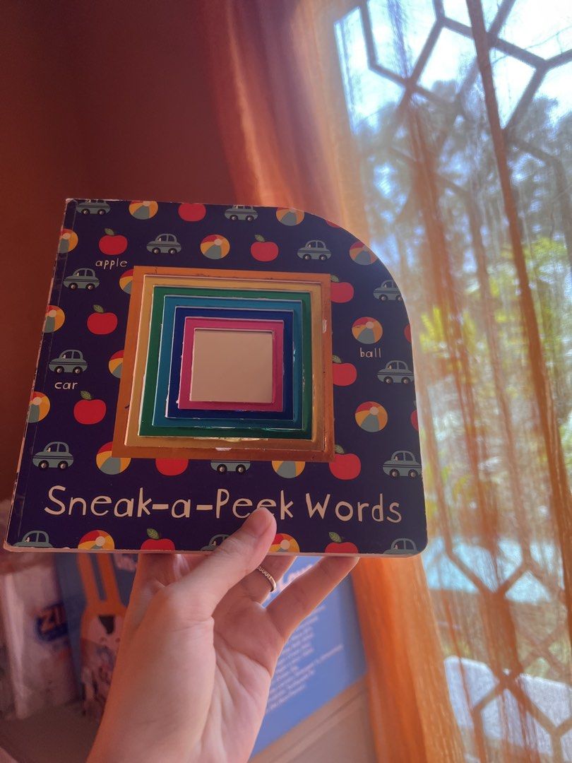 Sneak-a-Peek Words Board Book (Category: Children's Books) located in Quezon City. Submitted by joybautista05 (Listing ID 1465972573, Image 1). Description: - Title: Sneak-a-Peek Words Children's Board Book - Design: Dark blue cover with colorful cars, apples, and beach balls - Interactive feature: Die-cut layered window with a square mirror in the center - Build: Sturdy, chunky pages perfect for toddlers learning early vocabulary and handling by