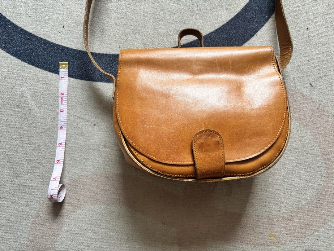 Tan Leather Saddle Crossbody Bag (Category: Cross-body Bags) located in Taguig. Submitted by narulover (Listing ID 1465977559, Image 3). Description: - Style: Structured tan leather saddle bag - Closure: Classic flap with magnetic tab strap - Features: Convenient top grab handle and adjustable shoulder strap with metal hardware - Condition: Shows natural scuffs and wear marks from regular use - Dimensions: Approximately 8 inches across x 7 inches