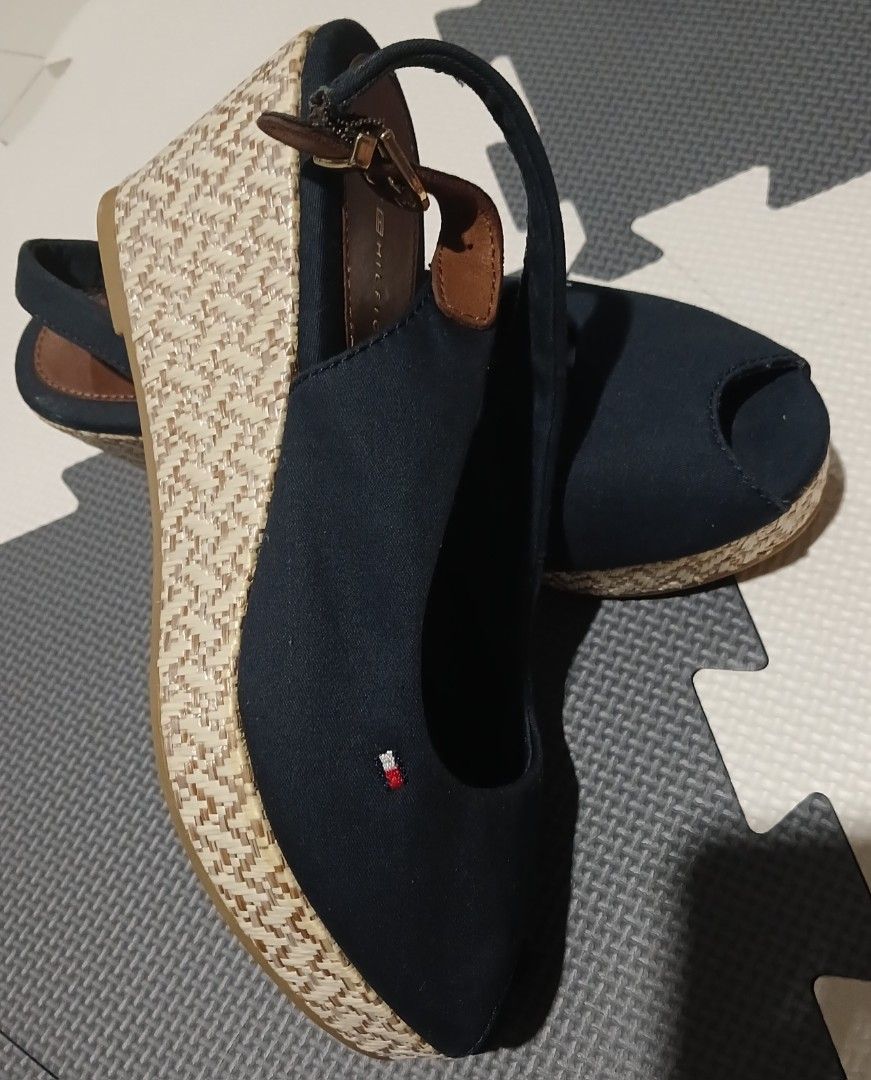 Tommy Hilfiger Navy Blue Wedge Sandals (Category: Sandals) located in Umingan. Submitted by mrobvariety (Listing ID 1465990125, Image 1). Description: - size: UK 3.5 - Brand: Tommy Hilfiger - Style: Open-toe wedge sandals with slingback strap and buckle closure - Color/Material: Navy blue canvas upper with dark brown leather details and woven jute platform - Details: Signature embroidered Tommy flag logo on the side - Fit/Condition: Comfortable f