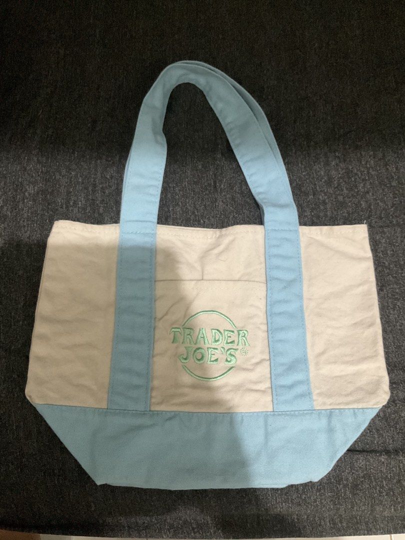 Trader Joe's Canvas Tote Bag Light Blue (Category: Tote Bags) located in Manila. Submitted by theklaaattteeerrr (Listing ID 1466057619, Image 1). Description: - 100% Authentic Trader Joe's canvas tote bag - Color: Off-white with light blue straps and bottom base - Branding: Distinctive green embroidered Trader Joe's logo on the front pocket - Material: Heavy-duty, durable cotton canvas - Design: Spacious main compartment with an open front pocket
