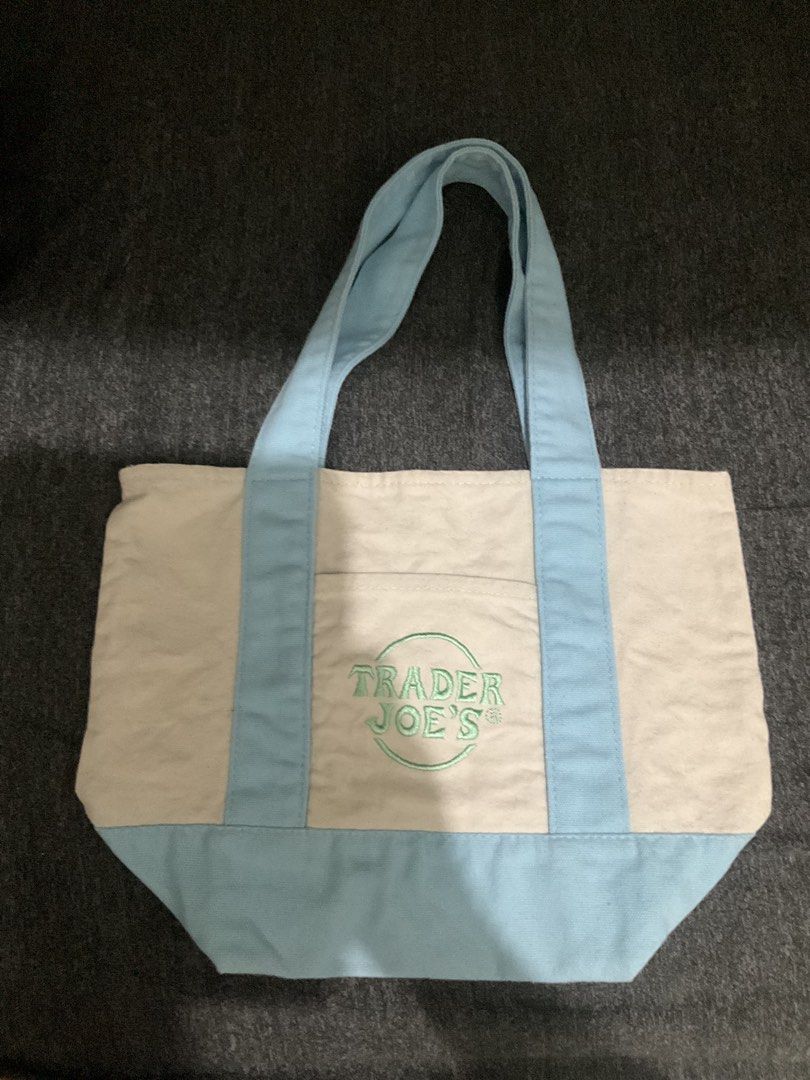 Trader Joe's Canvas Tote Bag Light Blue (Category: Tote Bags) located in Manila. Submitted by theklaaattteeerrr (Listing ID 1466057619, Image 2). Description: - 100% Authentic Trader Joe's canvas tote bag - Color: Off-white with light blue straps and bottom base - Branding: Distinctive green embroidered Trader Joe's logo on the front pocket - Material: Heavy-duty, durable cotton canvas - Design: Spacious main compartment with an open front pocket
