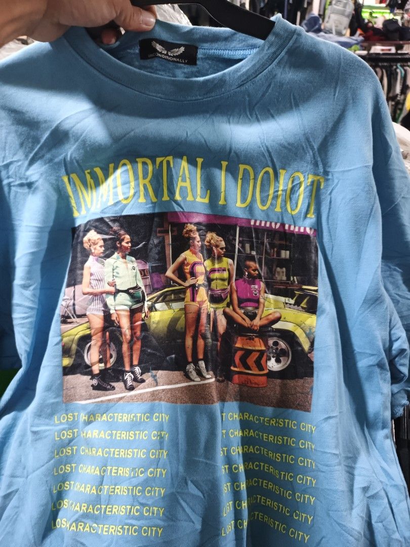 Unconditionally graphic tee (Category: Activewear) located in Odiongan. Submitted by thriftngo26 (Listing ID 1465962169, Image 1). Description: This is a light blue graphic t-shirt featuring a vintage-style photo print of four people standing in front of a yellow car, with the text "IMMORTAL IDIOT" above and repeated phrases like "LOST CHARACTERISTIC CITY" below.