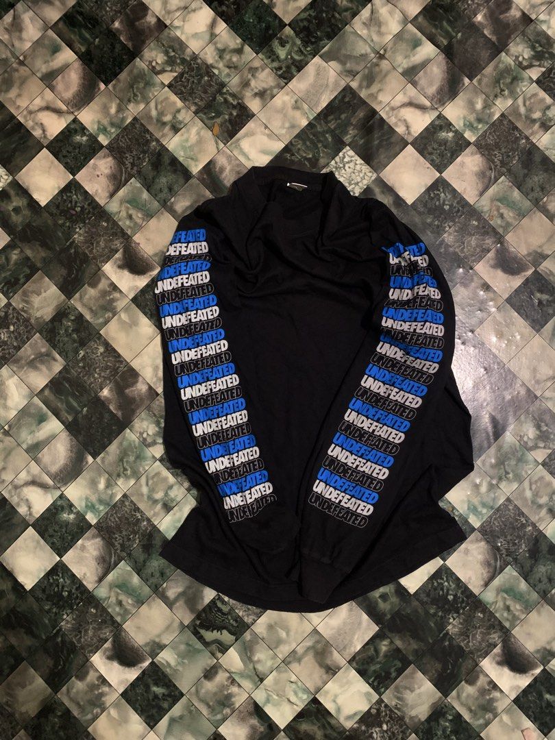 Undefeated Black Long Sleeve T-Shirt (Category: Tshirts & Polo Shirts ) located in Cebu City. Submitted by tangubrhia45277 (Listing ID 1466082349, Image 2). Description: - Brand: Undefeated - Item: Black long sleeve t-shirt with crew neck - Details: Blue and white logo text printed down both sleeves - Size: Small - Origin: Made in USA (Official licensed product tag included) - Condition: Clean fabric, well-maintained.