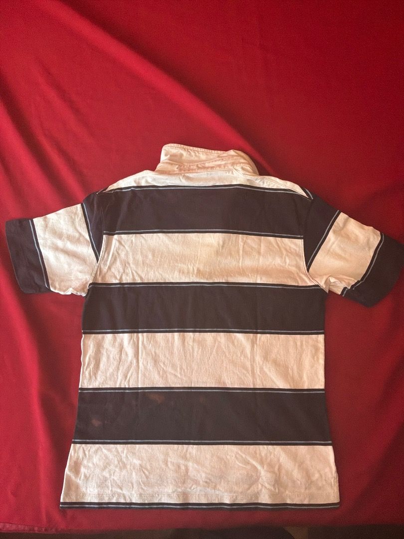 Uniqlo Polo. (Category: Formal Shirts) located in Tagum. Submitted by warmlion.40dc2c (Listing ID 1465988531, Image 2). Description: This short-sleeve rugby polo shirt features wide navy blue and white horizontal stripes accented with thin light blue borders. It has a classic white foldover collar, a two-button placket, and side-slit hems for a preppy, casual look. Note that there is faint reddish discoloration visible on the right midsection nav