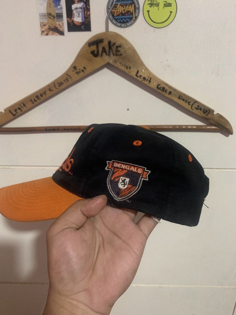 Vintage Cincinnati Bengals Snapback Hat (Category: Caps & Hats) located in Bauang. Submitted by jkjk32 (Listing ID 1466107778, Image 2). Description: - Authentic Cincinnati Bengals snapback cap - Color: Black with vibrant orange brim and matching snap closure - Features embroidered team graphics on the front and side panel - Classic retro green undervisor - Condition: Pre-owned, shows some wear and staining along the inner sweatband.