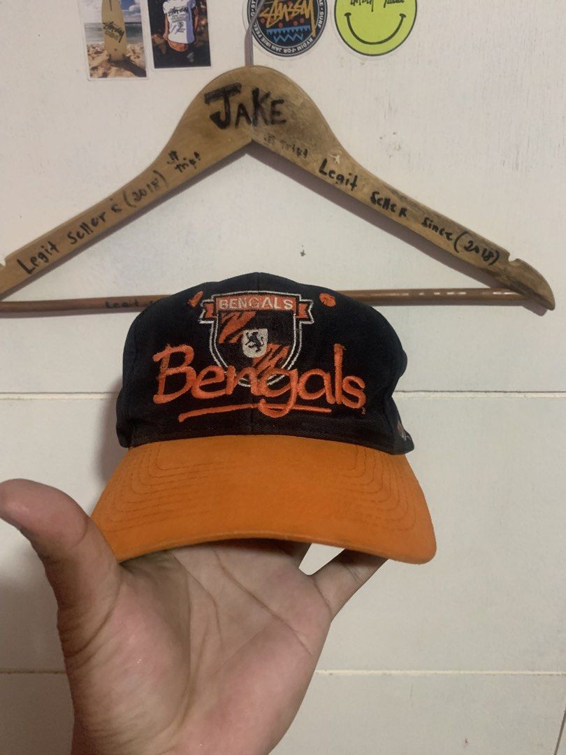 Vintage Cincinnati Bengals Snapback Hat (Category: Caps & Hats) located in Bauang. Submitted by jkjk32 (Listing ID 1466107778, Image 1). Description: - Authentic Cincinnati Bengals snapback cap - Color: Black with vibrant orange brim and matching snap closure - Features embroidered team graphics on the front and side panel - Classic retro green undervisor - Condition: Pre-owned, shows some wear and staining along the inner sweatband.