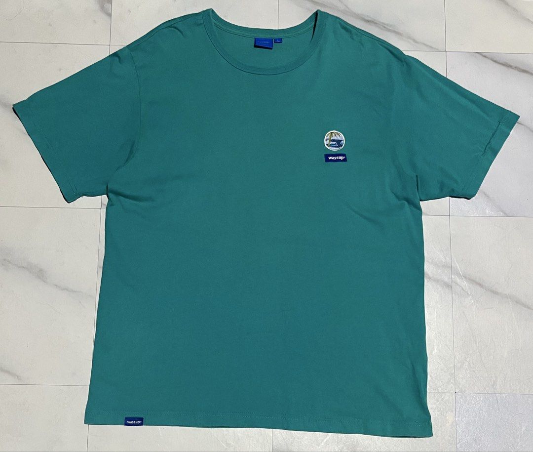 Wassup Teal T-Shirt Size L (Category: Tshirts & Polo Shirts ) located in Cavite. Submitted by christianzuuu (Listing ID 1466102790, Image 2). Description: - Brand: Wassup - Color: Teal green - Size: L (tag attached) - Design: Small left chest graphic with blue brand label, large white cursive print across the back - Details: Crew neck, short sleeves, small blue tag on bottom left hem - Condition: Brand new with tag.