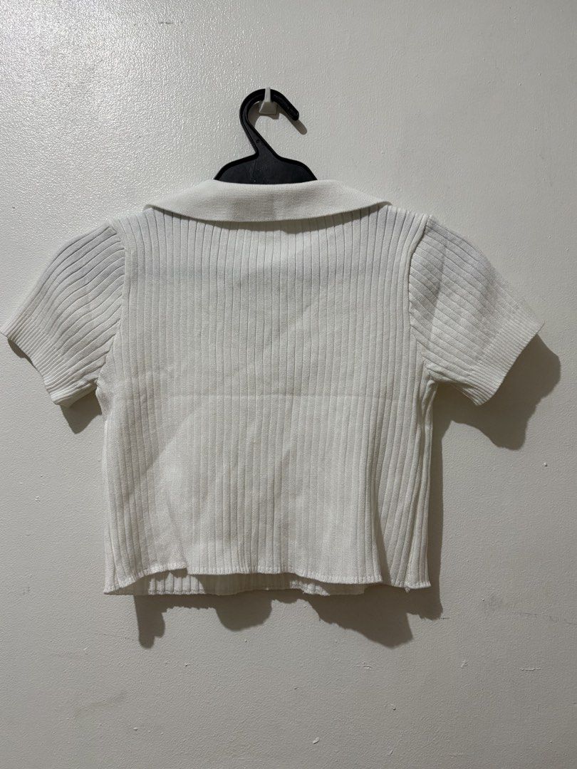 White ribbed polo crop top short sleeve (Category: Shirts) located in Manila. Submitted by nykji96 (Listing ID 1465963908, Image 2). Description: - Color: Clean solid white - Style: Collared V-neck short sleeve crop top - Material: Soft, stretchy ribbed knit fabric - Fit: Body-hugging, hits right above the waist - Condition: Excellent, no stains or loose threads - Versatility: Super easy to match with jeans or skirts for everyday wear.