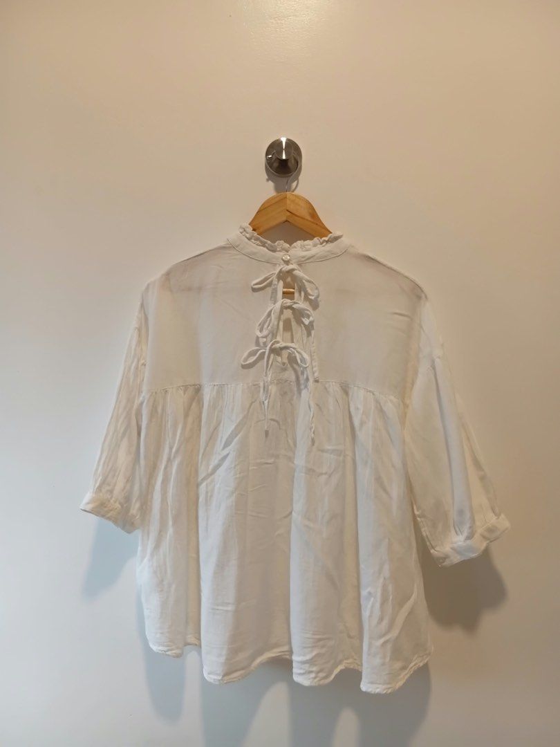 White ruffle neck tie back blouse M-L (Category: Blouses) located in Antipolo. Submitted by wisecat.4a7eea (Listing ID 1466040489, Image 2). Description: - Color: White - Size: Fits Medium to Large - Design: High ruffled neckline with single back button - Details: Cute back cutout with three ribbon ties and gathered front/back yoke - Sleeves: Mid-length with cuffs - Fabric: Lightweight and comfortable.