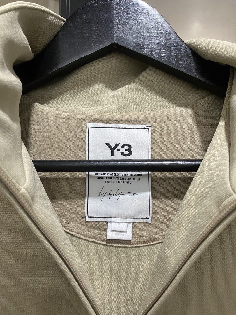 Y-3 Adidas Full Zip Track Jacket Beige Size M (Category: Coats, Jackets and Outerwear) located in Manila. Submitted by hell_market (Listing ID 1466119143, Image 2). Description: Beige Y-3 full zip track jacket by Yohji Yamamoto. Large bright orange Y-3 logo printed across the back. Stand-up collar, ribbed hem, ribbed cuffs, and zippered side pockets. YKK zippers. Made in China. Main material 100% polyamide, ribbing 88% polyamide and 12% elastane,