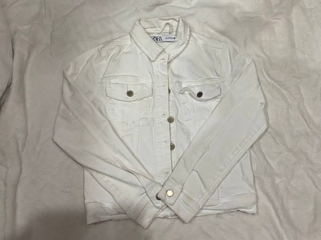 Zara White Denim Jacket (Category: Coats, Jackets and Outerwear) located in Manila. Submitted by lovelypreloved1497 (Listing ID 1466102545, Image 1). Description: - Brand: Zara - Size: L (EUR L, USA L, MEX 30) - Color: White denim - Features: Classic button-down front, chest pockets, metal buttons - Flaws: Minor yellow stain near hem and button area, small tear on the back fabric - Origin: Made in Bangladesh.