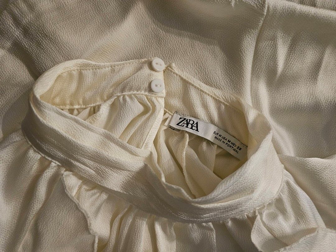 Zara White Ruffled Long Sleeve Blouse Size M (Category: Longsleeves) located in Manila. Submitted by john.tulalian (Listing ID 1466126178, Image 2). Description: - Brand: Zara - Size: EUR M / USA M / MEX 28 - Color: Classic White - Material: Textured fabric (Made in Portugal) - Design: High neckline with back double-button closure - Details: Long sleeves with ruffled cuffs and layered ruffle hemline - Condition: Excellent / Ready to wear -Negotia