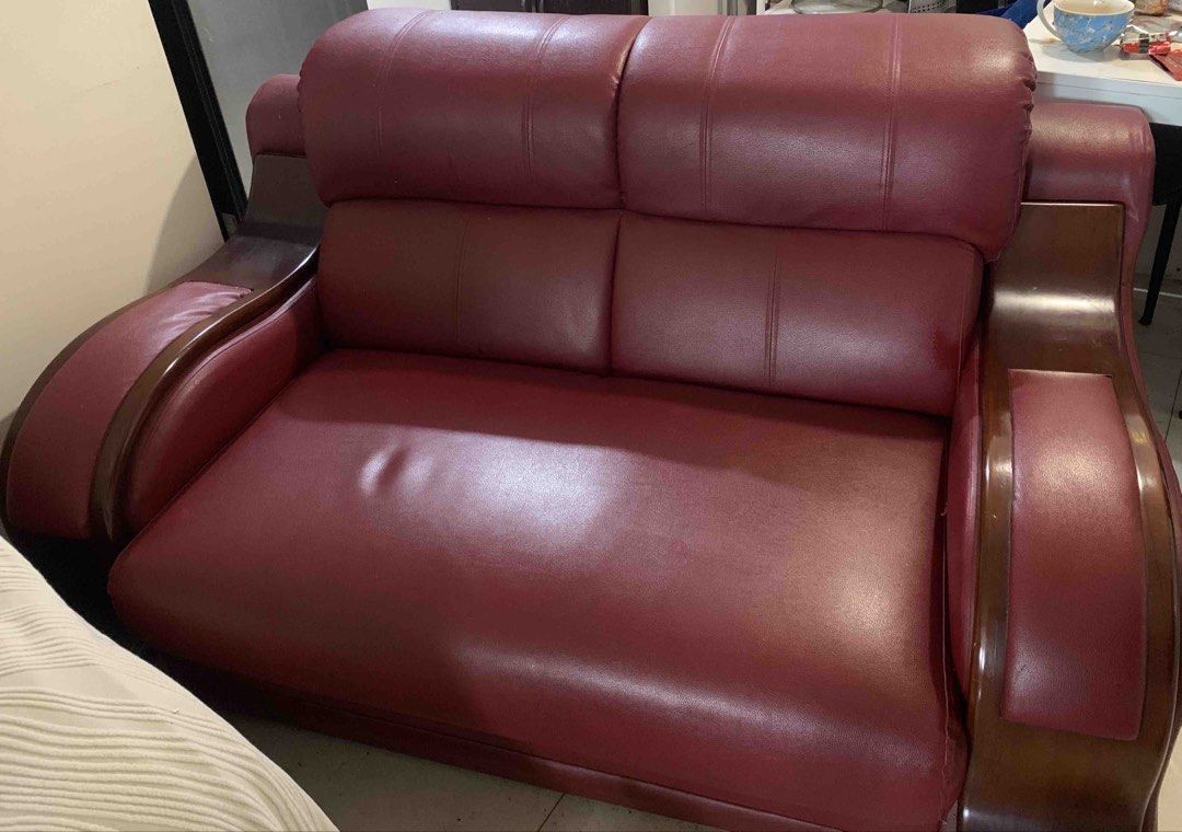 2-Seater Sofa with Wooden Armrests (Category: Sofas) located in Quezon City. Submitted by rencizuniga (Listing ID 1466223360, Image 1). Description: - Type: 2-seater faux leather sofa - Color: Deep red / maroon - Features: Thick cushioned backrest and seat, solid dark wood armrests with built-in flat panels - Condition: Sturdy build with a minor depression on the left seat cushion - Ideal for: Living rooms or office spaces Issue: minor scratches 