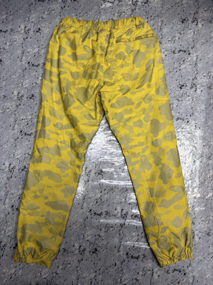 A Bathing Ape Yellow Camo Jogger Pants BAPE (Category: Joggers) located in Manila. Submitted by raven236 (Listing ID 1466195614, Image 2). Description: - Bright yellow BAPE camo track pants - Distinctive all-over pattern with white A BATHING APE leg branding - Elastic waistband with button closure and cuffed ankles - Features a convenient back pocket - Lightweight fabric, ideal for streetwear.