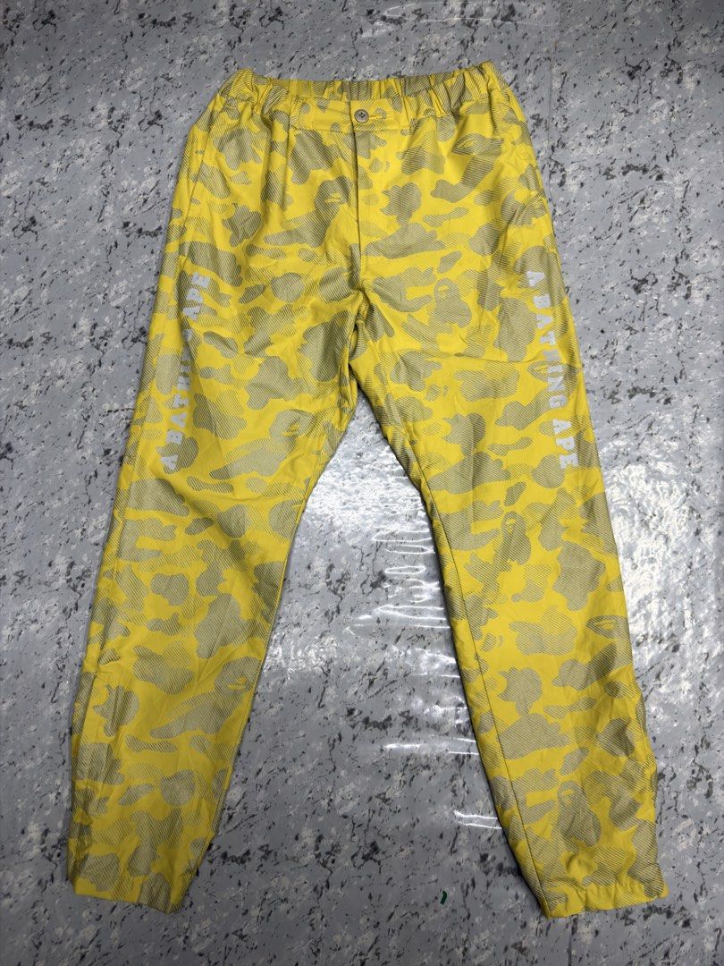 A Bathing Ape Yellow Camo Jogger Pants BAPE (Category: Joggers) located in Manila. Submitted by raven236 (Listing ID 1466195614, Image 1). Description: - Bright yellow BAPE camo track pants - Distinctive all-over pattern with white A BATHING APE leg branding - Elastic waistband with button closure and cuffed ankles - Features a convenient back pocket - Lightweight fabric, ideal for streetwear.