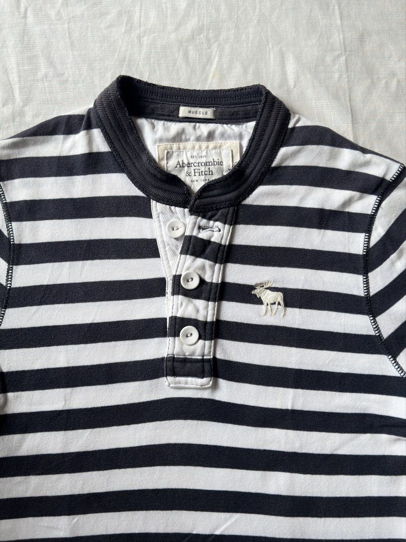 ABERCOMBIE (Category: Tshirts & Polo Shirts ) located in Davao. Submitted by kelsocool (Listing ID 1466256024, Image 3). Description: Abercrombie & Fitch Striped Short-Sleeve Henley Dimes (inch): 24 - length 20 - width 8.5 - sleeve color rate: 9/10 no issue good condition Model: 5’5 ft/ 54 kg Description: Y2K preppy striped henley with contrast navy collar, branded white buttons, and embroidered moose logo chest hit..