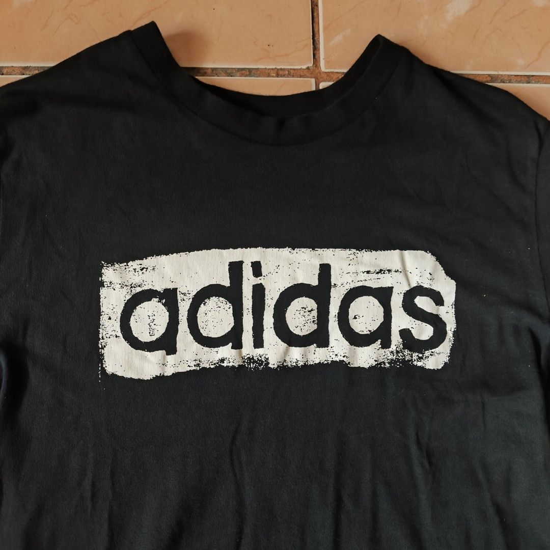 Adidas Black Graphic T-Shirt Size M (Category: Tshirts & Polo Shirts ) located in Pili. Submitted by emmanuelmotos (Listing ID 1466176196, Image 3). Description: - Brand: Adidas - Color: Black with large white distressed brushstroke logo - Size: Medium (Standard fit) - Material: 100% Cotton - Details: Crew neck, short sleeves, small Adidas logo tag on left sleeve - Production Date: 09/20 - Condition: Excellent, great for casual streetwear.