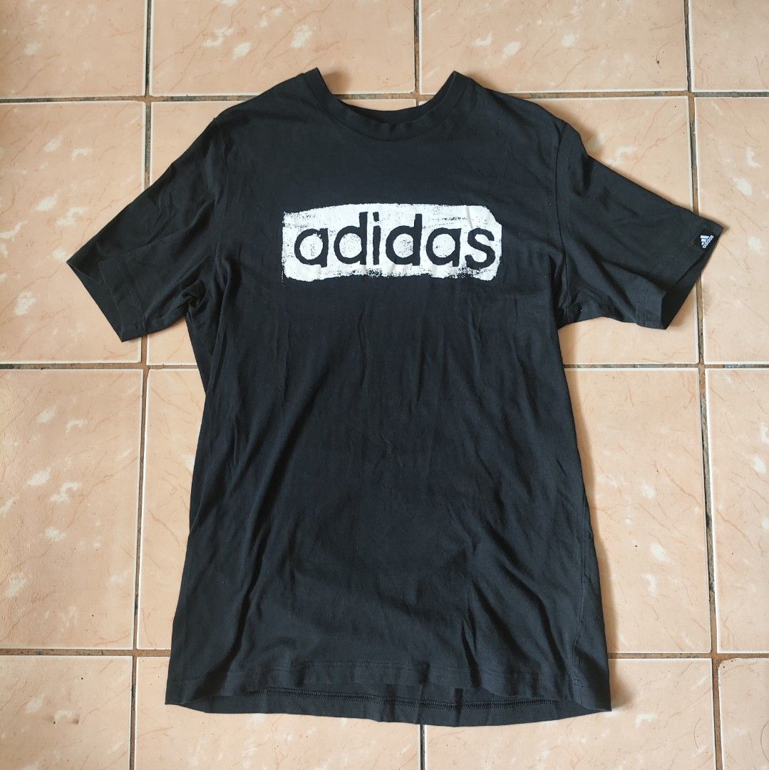 Adidas Black Graphic T-Shirt Size M (Category: Tshirts & Polo Shirts ) located in Pili. Submitted by emmanuelmotos (Listing ID 1466176196, Image 1). Description: - Brand: Adidas - Color: Black with large white distressed brushstroke logo - Size: Medium (Standard fit) - Material: 100% Cotton - Details: Crew neck, short sleeves, small Adidas logo tag on left sleeve - Production Date: 09/20 - Condition: Excellent, great for casual streetwear.