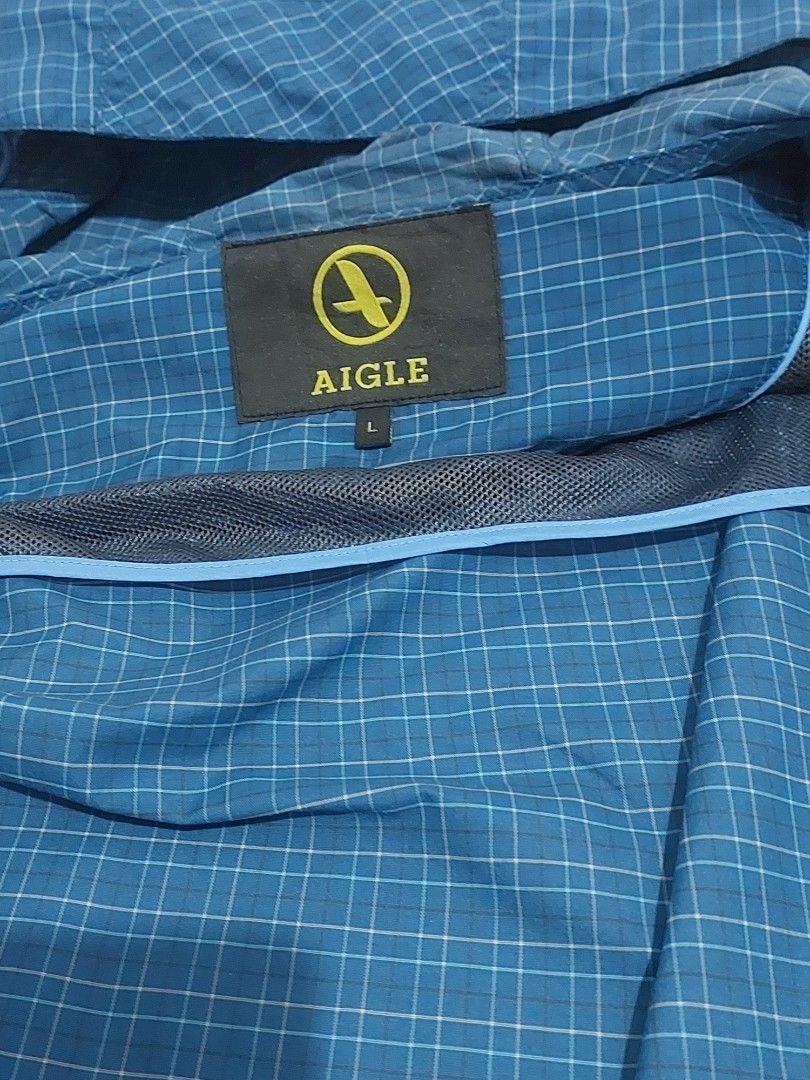 Aigle Blue Plaid Hooded Jacket Size L (Category: Coats, Jackets and Outerwear) located in Naga. Submitted by ravenmandm (Listing ID 1466278598, Image 3). Description: Blue plaid hooded jacket by Aigle. Size L on the tag. Full zip front closure with grey zipper tape. Mesh lining inside. Elastic cuffs at the sleeves. Two front pockets with zippers. Lightweight outdoor layer, easy to pack along. Issue: small hole on the hood part.