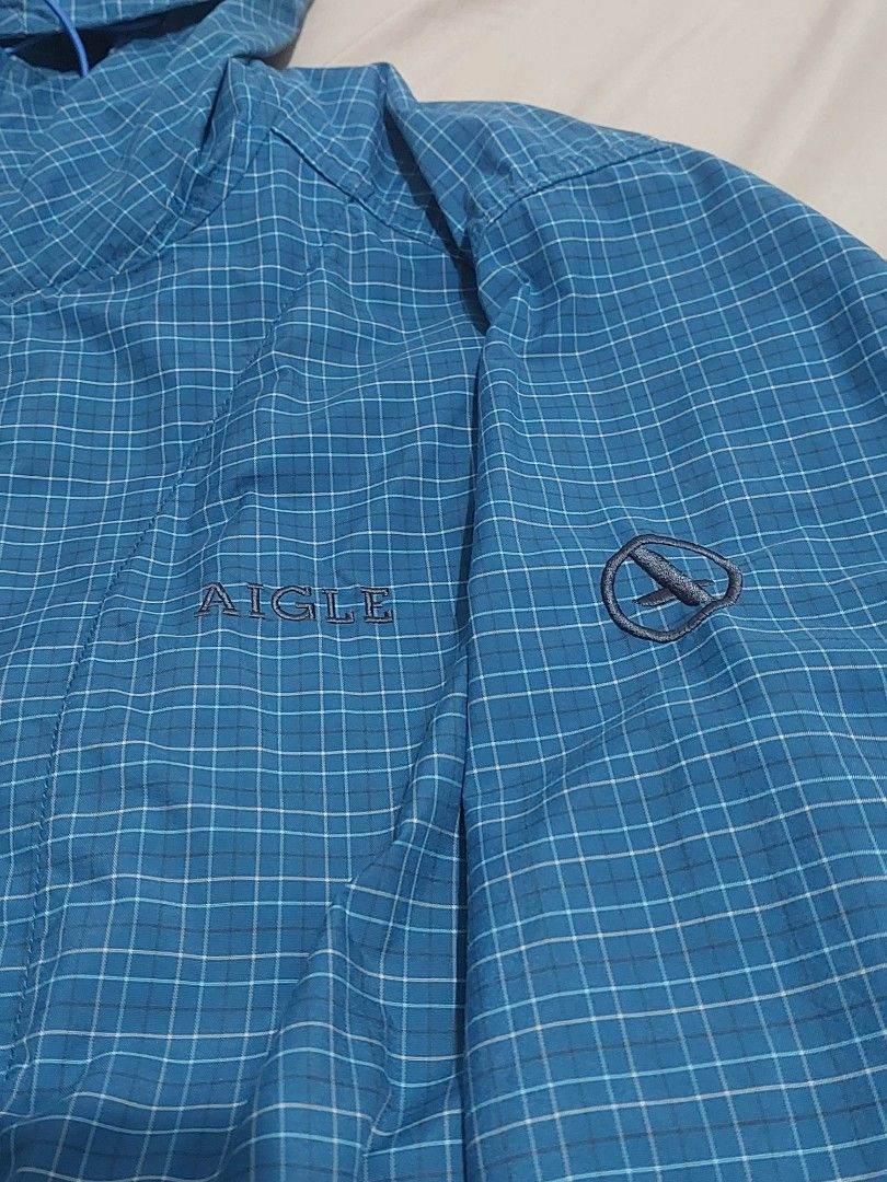 Aigle Blue Plaid Hooded Jacket Size L (Category: Coats, Jackets and Outerwear) located in Naga. Submitted by ravenmandm (Listing ID 1466278598, Image 2). Description: Blue plaid hooded jacket by Aigle. Size L on the tag. Full zip front closure with grey zipper tape. Mesh lining inside. Elastic cuffs at the sleeves. Two front pockets with zippers. Lightweight outdoor layer, easy to pack along. Issue: small hole on the hood part.