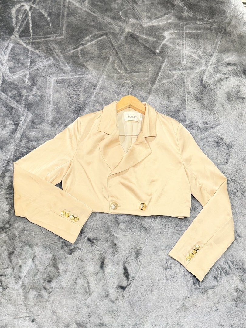 BANSUU Beige Cropped Blazer Size M (Category: Coats, Jackets and Outerwear) located in Manila. Submitted by yeti_it (Listing ID 1466258405, Image 2). Description: - Brand: BANSUU - Item: Cropped Blazer - Color: Beige - Material: Smooth satin - Size: Medium (tag attached) - Details: Double-breasted front, lapel collar, and luxurious gold-toned embossed buttons on the front and cuffs - Condition: Clean fabric with a smooth texture.