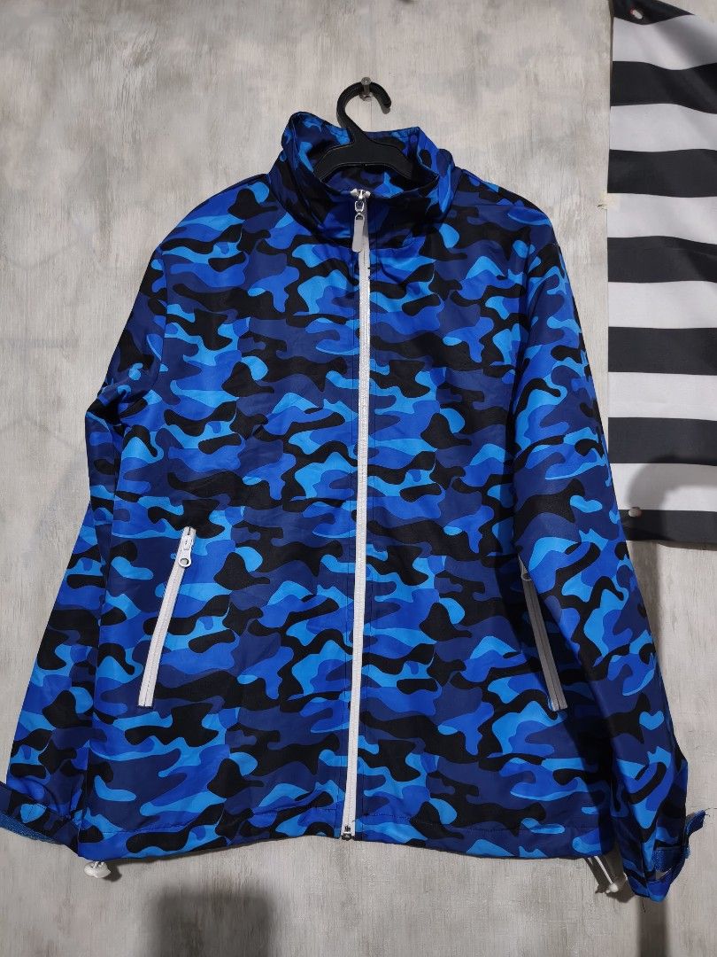 Blue Camo Winning Team Windbreaker Jacket (Category: Coats, Jackets and Outerwear) located in Baguio. Submitted by fordaluvofthrift2600 (Listing ID 1466168556, Image 1). Description: - Color/Pattern: Blue and black camo print - Closures & Pockets: White front zipper and functional side zip pockets - Hem: Adjustable drawstring for a customized fit - Back Detail: Embroidered 'Winning Team' lettering in silver with a green hash symbol and signature 