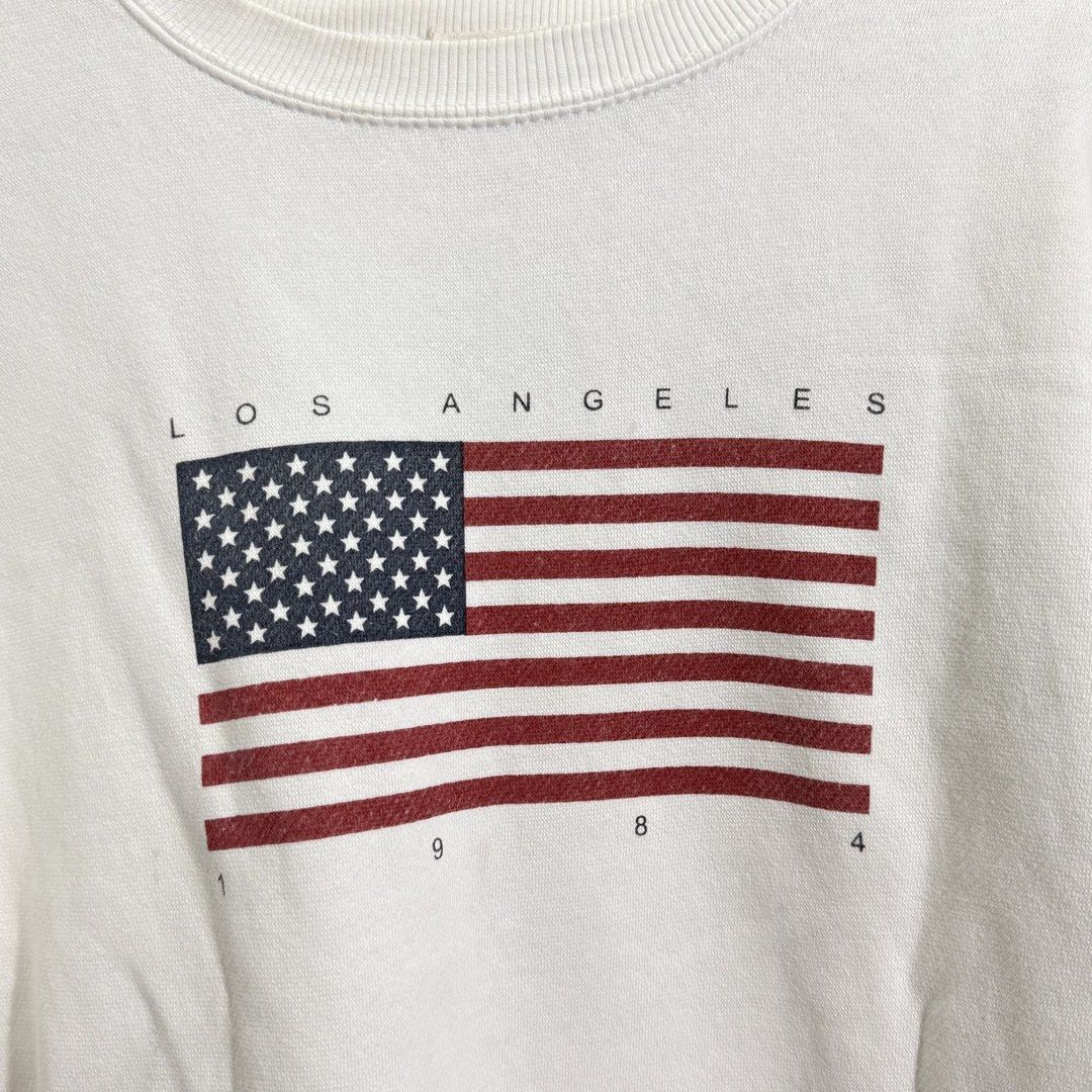Brandy Melville Sweatshirt (Category: Coats, Jackets and Outerwear) located in Manila. Submitted by she_alice (Listing ID 1466325387, Image 2). Description: - Color: White -Size: Small (Oversized) can fit up to Large - Design: Vintage LA graphic with American flag and '1984' print - Super pretty in actual. 💬 Feel free to message me for any questions 🛵 Can be shipped via Lalamove .