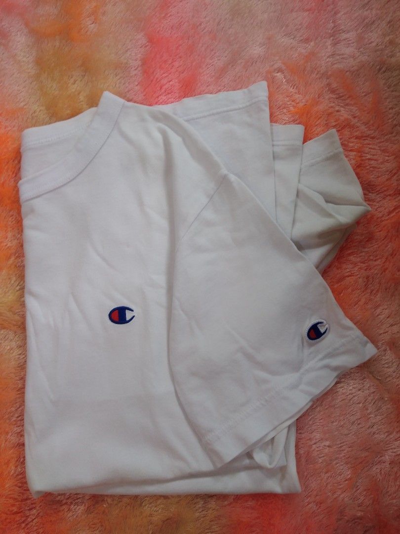 Champion White T-Shirt Medium>Width 19/Length 27 (Category: Shirts) located in San Isidro, Davao Oriental. Submitted by nelthrift30 (Listing ID 1466179771, Image 3). Description: - Brand: Champion - Color: White - Size: Medium - Design: Classic crew neck with short sleeves - Details: Small embroidered Champion logo patch on the chest and left sleeve - Condition/Tag: Authentic American Athleticwear interior tag - Style: Clean, minimalist, and easy