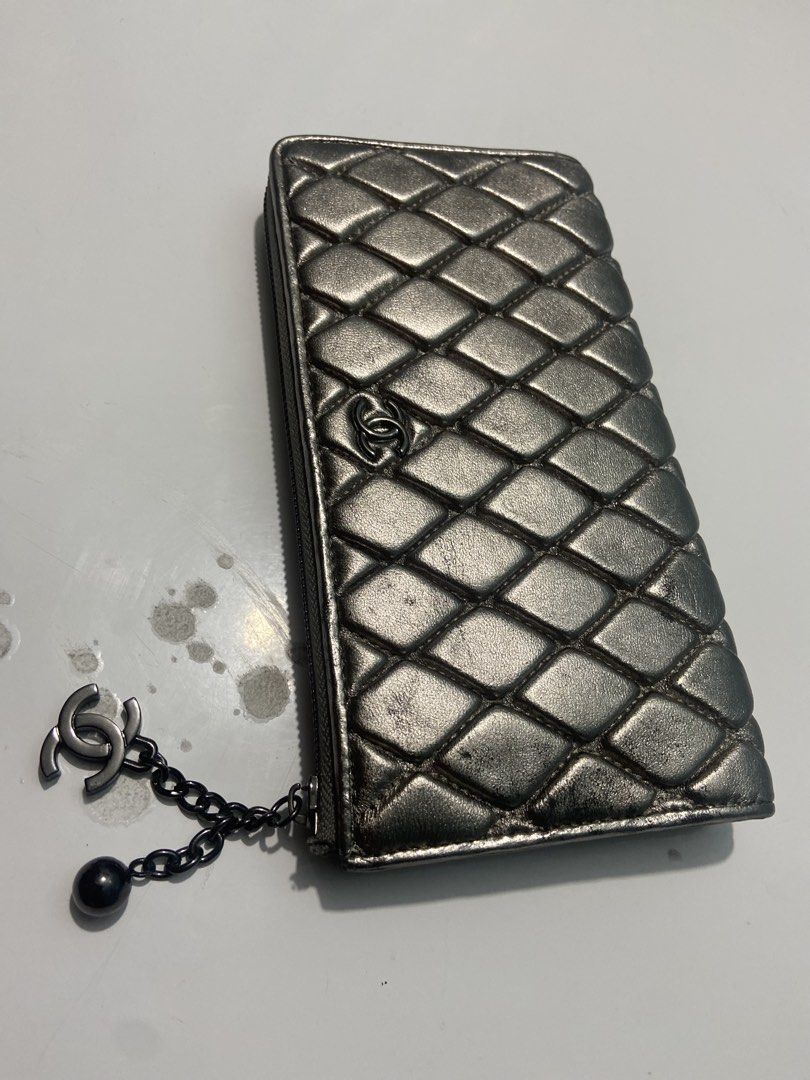 Chanel Quilted Metallic Silver Zip Wallet with CC Charm (Category: Wallets & Card holders) located in Manila. Submitted by kentjohnz. (Listing ID 1466230902, Image 1). Description: Chanel quilted long zip wallet in metallic silver leather. Dark ruthenium hardware with a hanging CC logo and ball charm. Zip-around closure with normal signs of wear on the quilted leather surface and edges. Classic interlocking CC logo on the front. Functional zipper