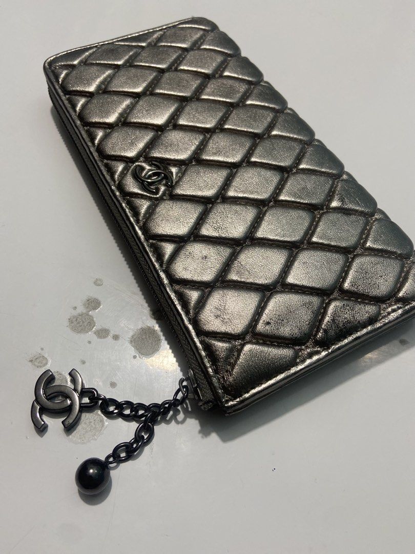 Chanel Quilted Metallic Silver Zip Wallet with CC Charm (Category: Wallets & Card holders) located in Manila. Submitted by kentjohnz. (Listing ID 1466230902, Image 3). Description: Chanel quilted long zip wallet in metallic silver leather. Dark ruthenium hardware with a hanging CC logo and ball charm. Zip-around closure with normal signs of wear on the quilted leather surface and edges. Classic interlocking CC logo on the front. Functional zipper