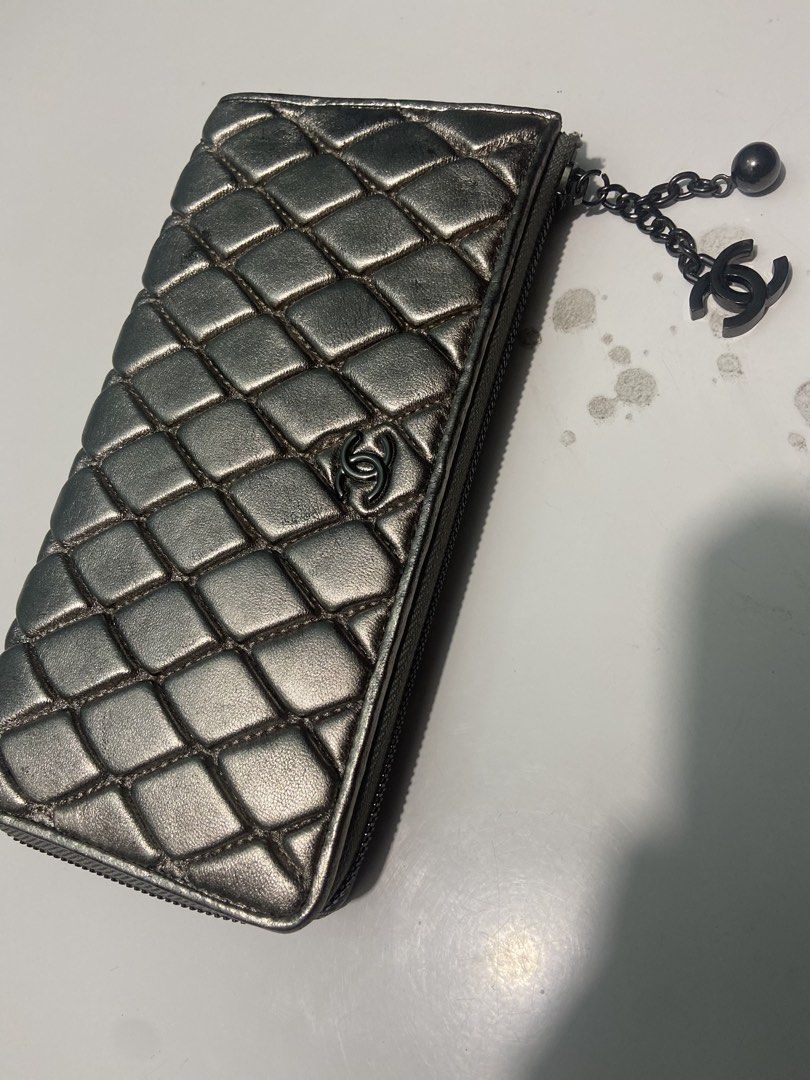 Chanel Quilted Metallic Silver Zip Wallet with CC Charm (Category: Wallets & Card holders) located in Manila. Submitted by kentjohnz. (Listing ID 1466230902, Image 2). Description: Chanel quilted long zip wallet in metallic silver leather. Dark ruthenium hardware with a hanging CC logo and ball charm. Zip-around closure with normal signs of wear on the quilted leather surface and edges. Classic interlocking CC logo on the front. Functional zipper
