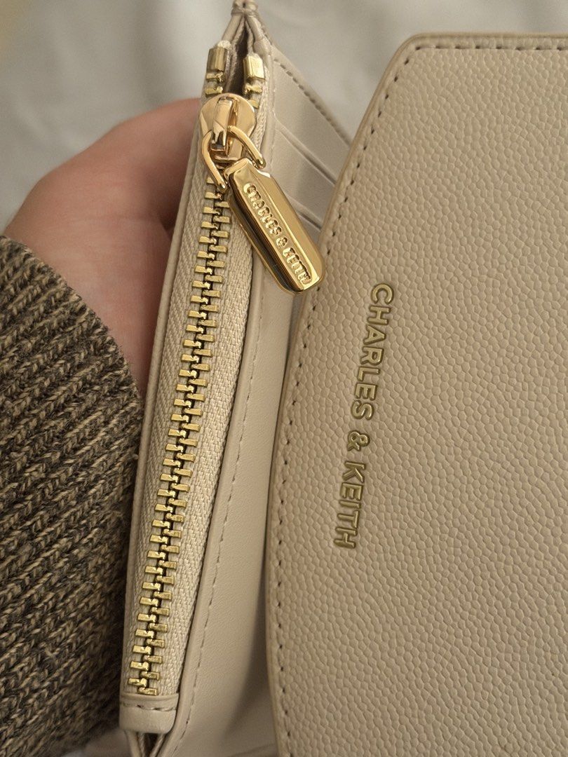 Charles & Keith Beige Trifold Wallet (Category: Wallets & Card holders) located in Las Pinas. Submitted by idontneedtheseanm (Listing ID 1466173761, Image 2). Description: - Brand: Charles and Keith - Color: Beige with textured finish - Hardware: Elegant gold-tone hardware and zipper pull - Closure: Secure snap button closure - Interior: Multiple card slots and a dedicated coin compartment - Size: Compact, fits easily into small bags - Condition: