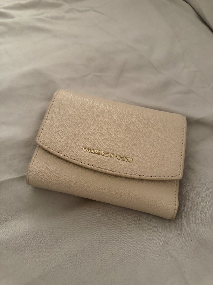 Charles & Keith Beige Trifold Wallet (Category: Wallets & Card holders) located in Las Pinas. Submitted by idontneedtheseanm (Listing ID 1466173761, Image 1). Description: - Brand: Charles and Keith - Color: Beige with textured finish - Hardware: Elegant gold-tone hardware and zipper pull - Closure: Secure snap button closure - Interior: Multiple card slots and a dedicated coin compartment - Size: Compact, fits easily into small bags - Condition: