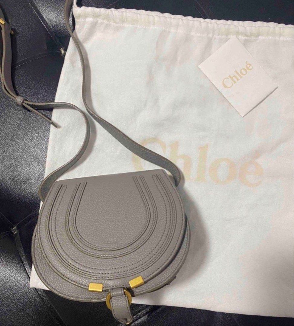 Chloé Marcie Saddle Bag Grey (Category: Luxury Bags & Wallets) located in Manila. Submitted by decluterthings888 (Listing ID 1466335614, Image 1). Description: Chloé Marcie saddle bag in a soft grey shade. Textured calfskin leather, horseshoe stitch detailing on the flap, antique gold hardware. Adjustable crossbody strap. Front flap closure with slip pocket underneath. Comes with original white dust bag and branded card. Clean interior and exteri